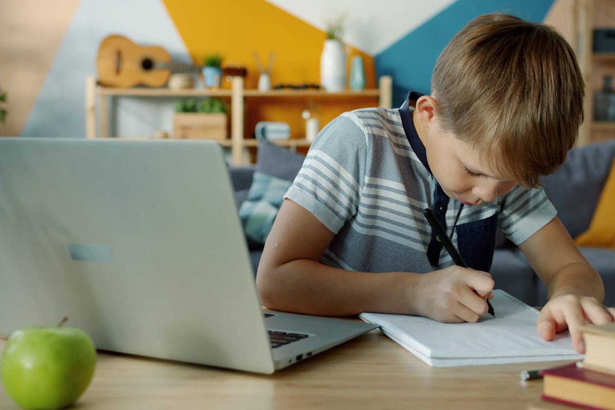 Jeune garcon etudiant devant un ordinateur portable avec un cahier
